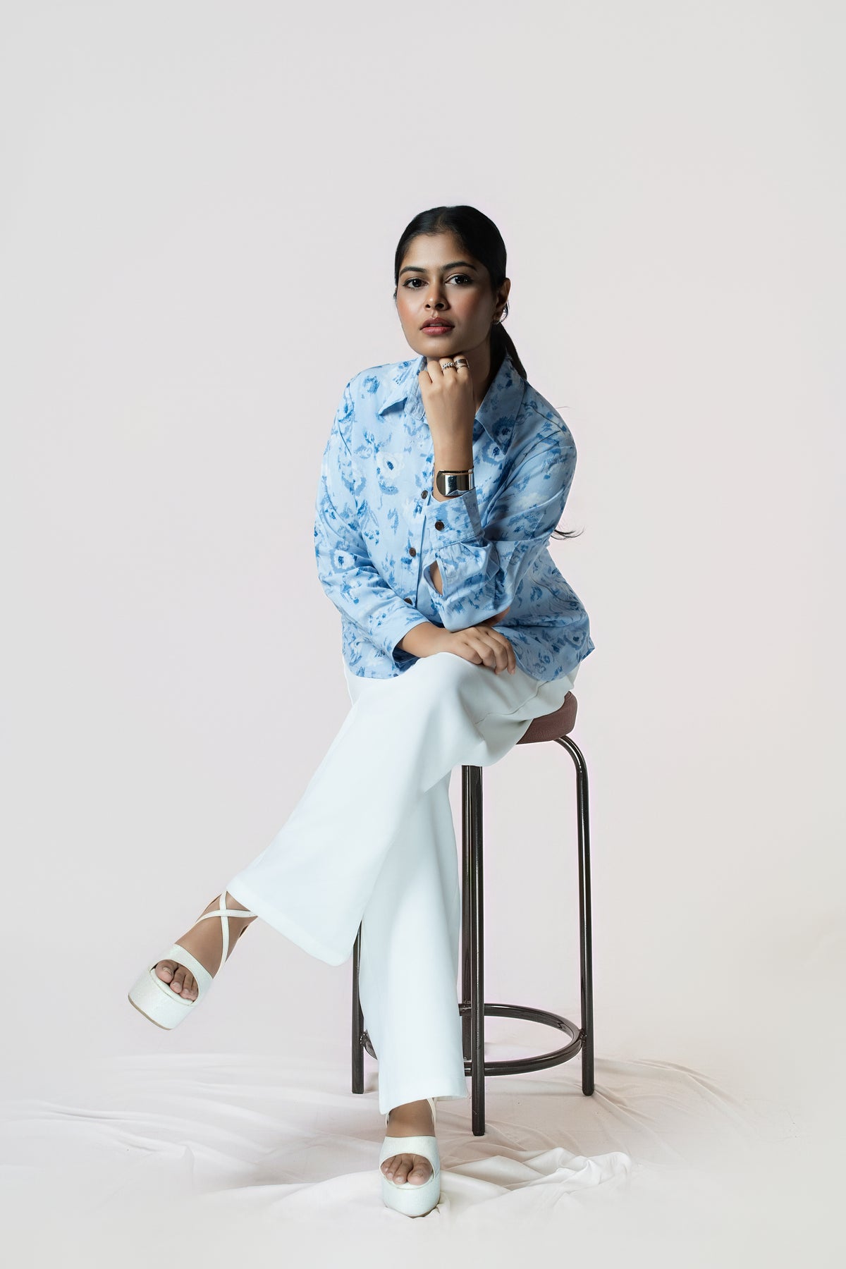 Skyline Bloom Shirt: light blue floral-print long-sleeve shirt, worn with white wide-leg trousers, seated close-up view