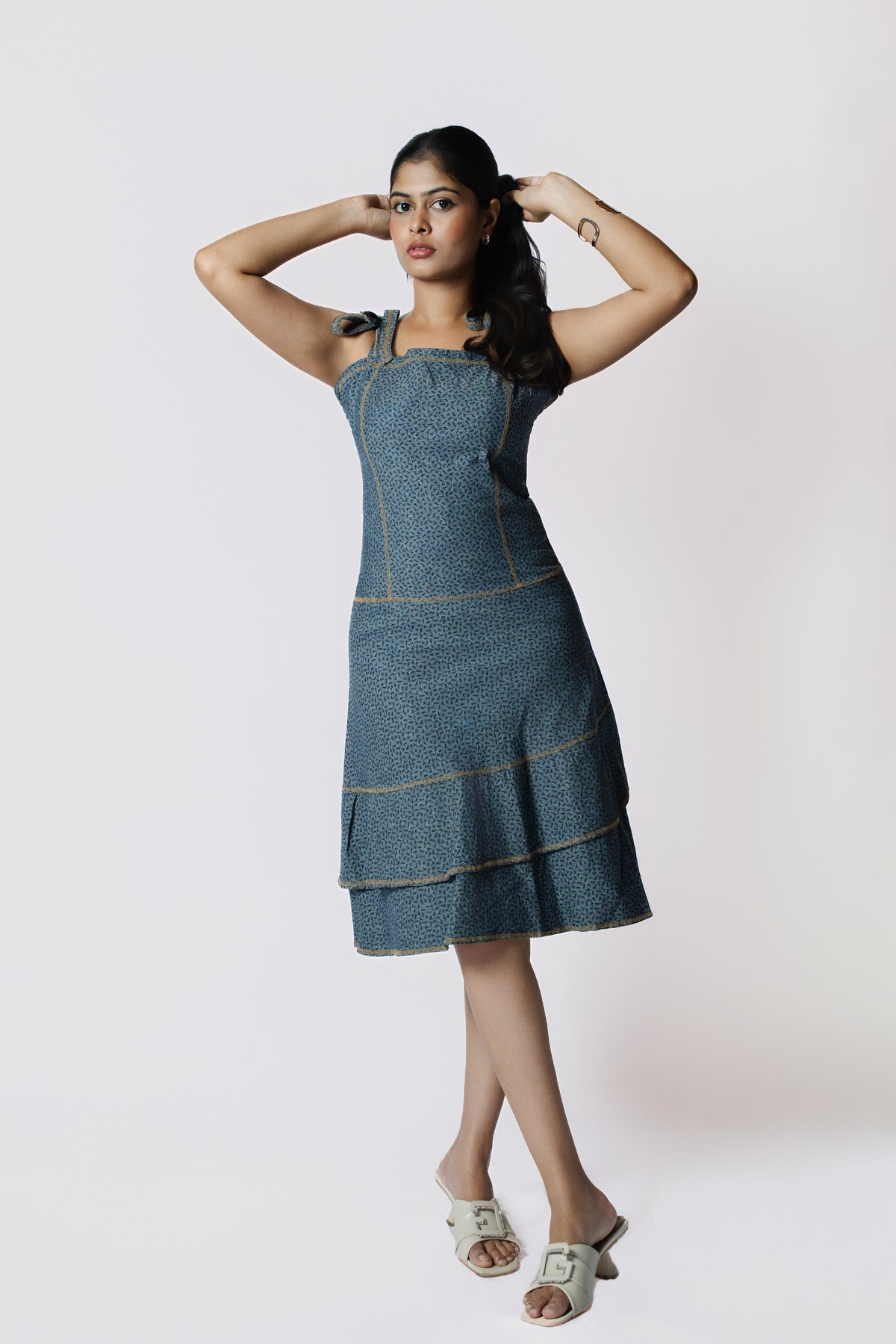 Indigo Whisper Tiered Dress: denim-blue sleeveless dress with tie shoulder straps and a tiered ruffle hem, front view, arms raised